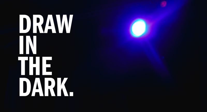 An image of a blue light shining over a dark room from a floor perspective. Bold, white text to the left of the light says "DRAW IN THE DARK." in all capital letters. 