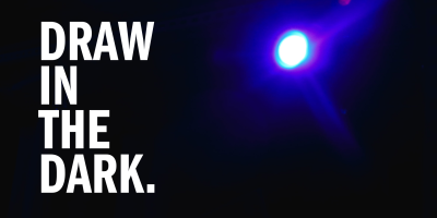An image of a blue light shining over a dark room from a floor perspective. Bold, white text to the left of the light says "DRAW IN THE DARK." in all capital letters. 